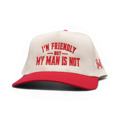 A red and off-white snapback cap with the text 'I'M FRIENDLY BUT MY MAN IS NOT' embroidered in red on the front, and a small red embroidered logo on the side, shown on a white background.