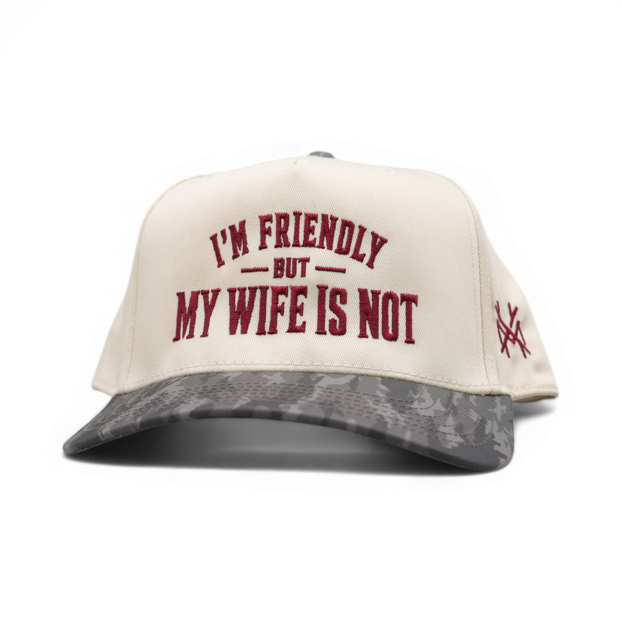 An off-white snapback cap with a gray camouflage patterned visor, featuring the text 'I'M FRIENDLY BUT MY WIFE IS NOT' embroidered in dark red on the front.
