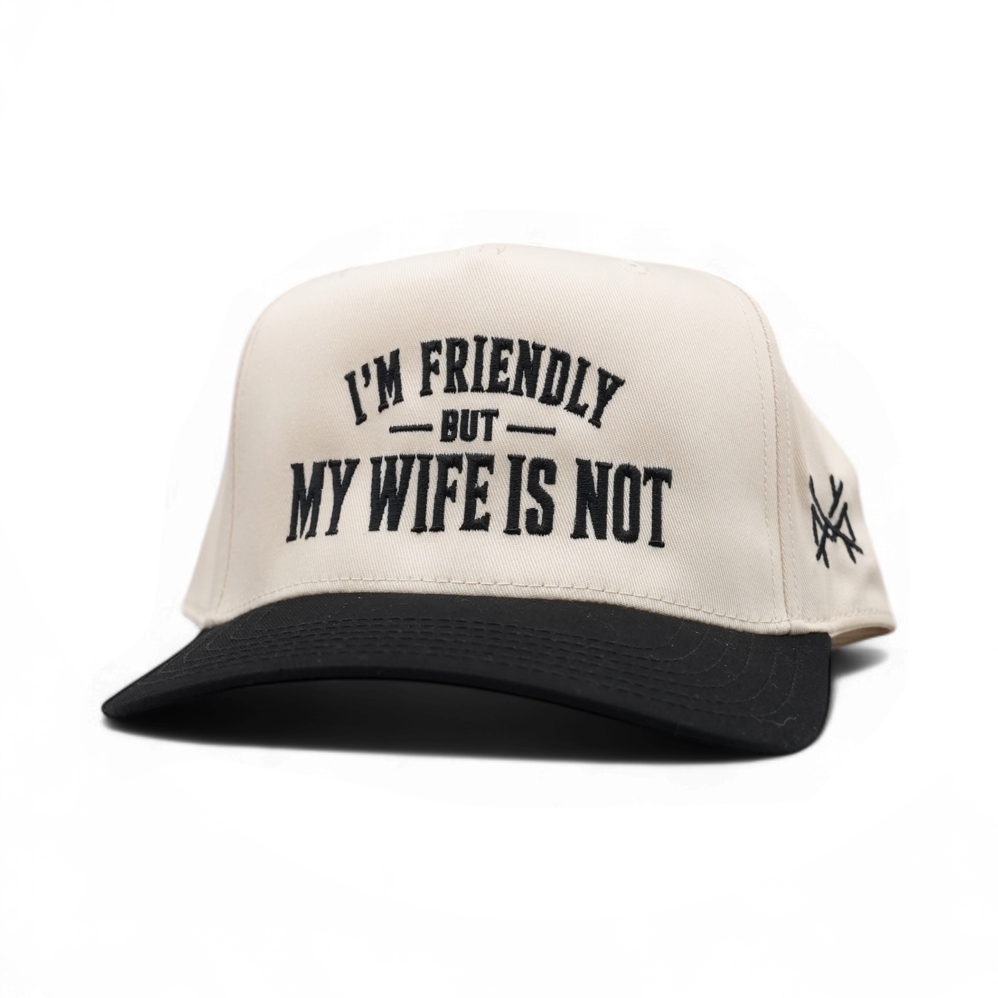 An off-white and black trucker-style cap with the text 'I'M FRIENDLY BUT MY WIFE IS NOT' embroidered on the front, shown on a plain white background.