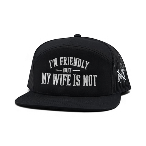 A black trucker hat with white embroidered text reading 'I'M FRIENDLY BUT MY WIFE IS NOT' on the front panel, shown against a plain white background.