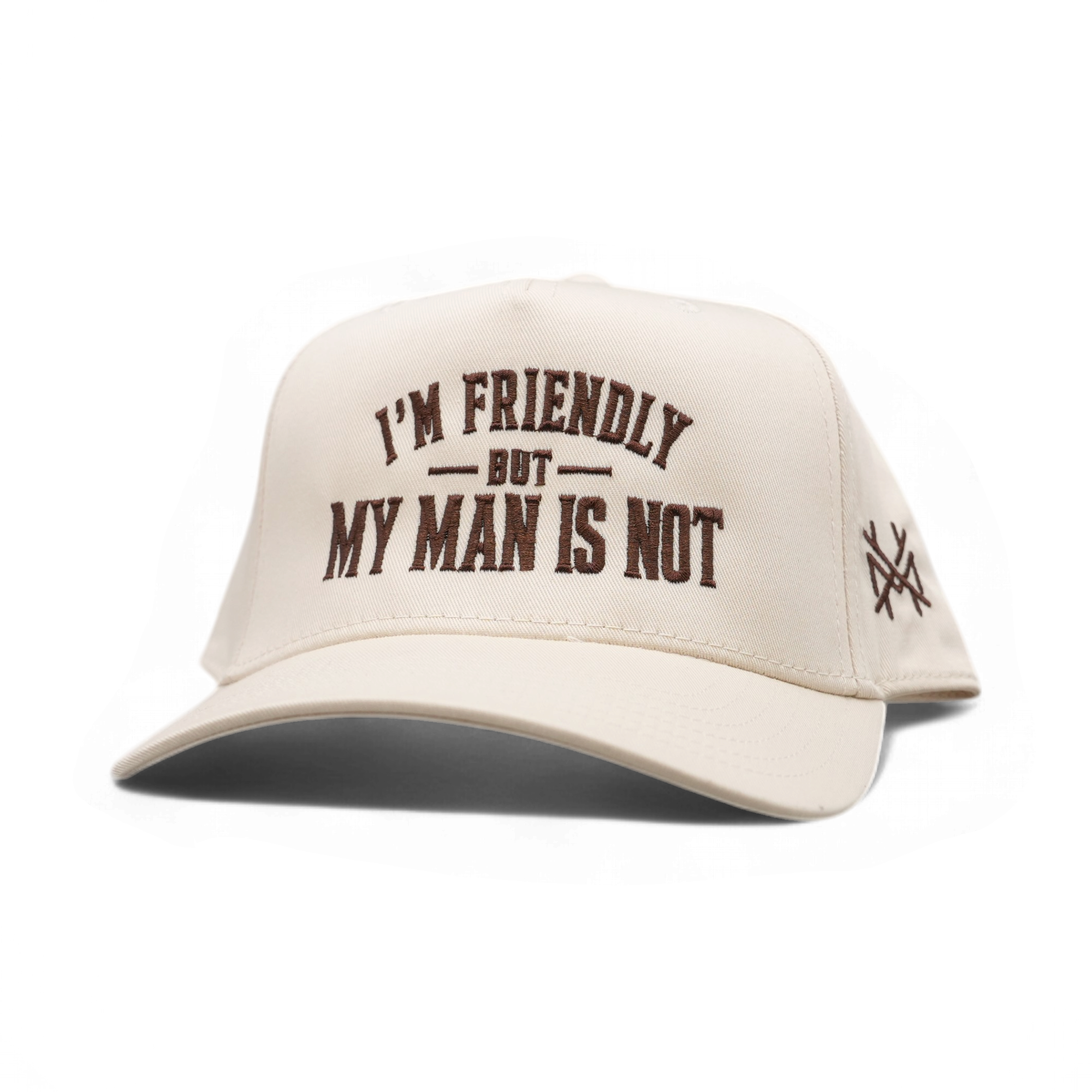 An off-white baseball cap with dark brown embroidered text reading 'I'M FRIENDLY BUT MY MAN IS NOT' on the front, and a small crossed-objects logo on the side, shown on a plain white background.