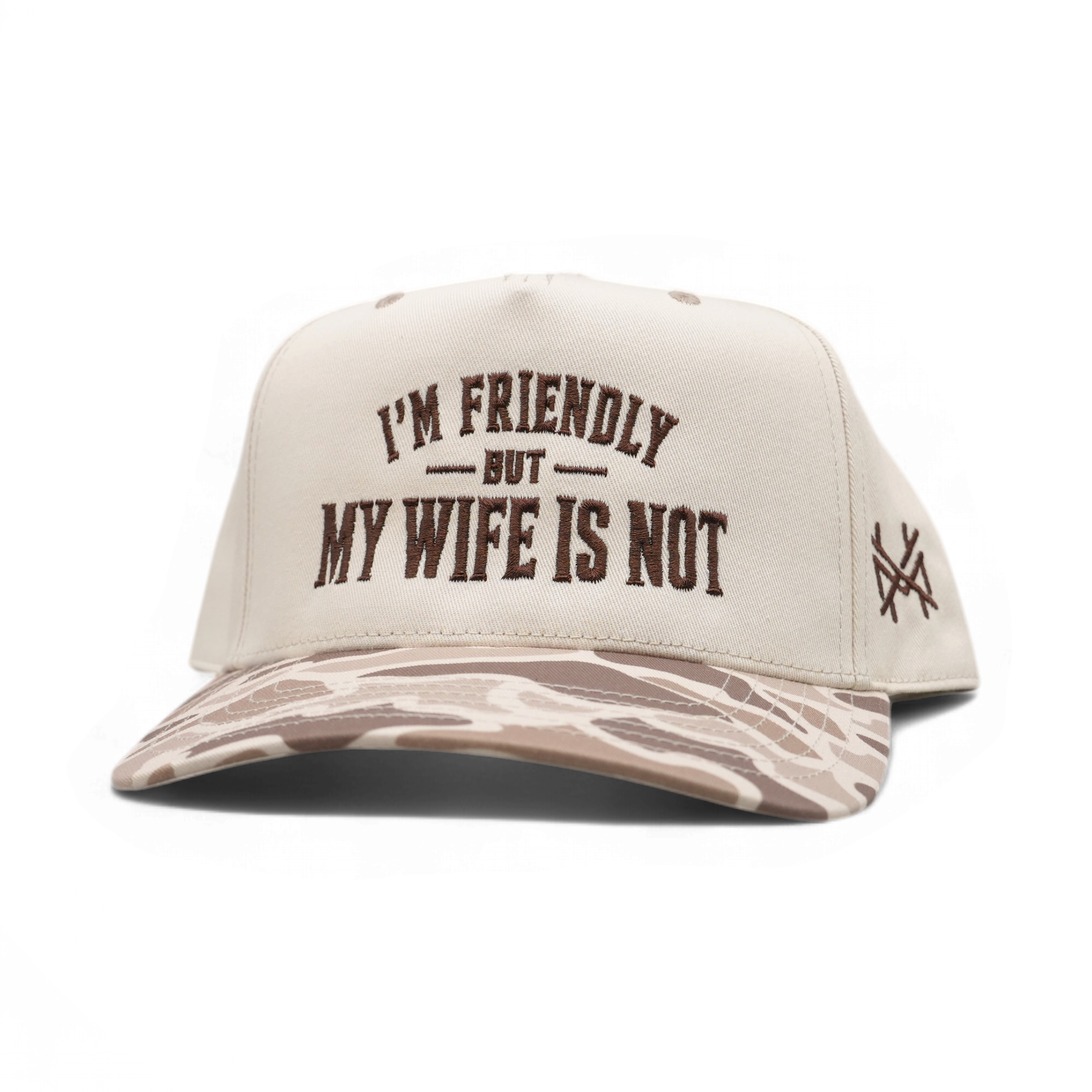 A beige snapback cap with a brown camouflage patterned brim, featuring the text 'I'M FRIENDLY BUT MY WIFE IS NOT' embroidered on the front and a small crossed-flags style logo on the side.