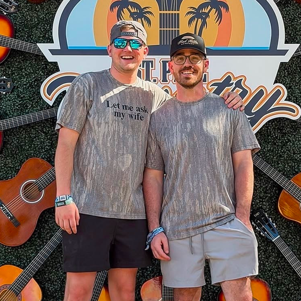 Mad Hatter Co. founders in front of a guitar wall at a country music festival