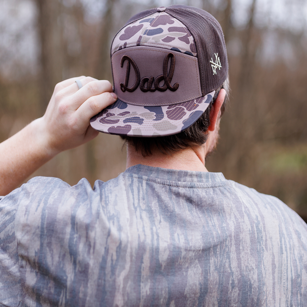 Man wearing a camo Mad Hatter Co. 7-panel hat with raised Dad embroidery