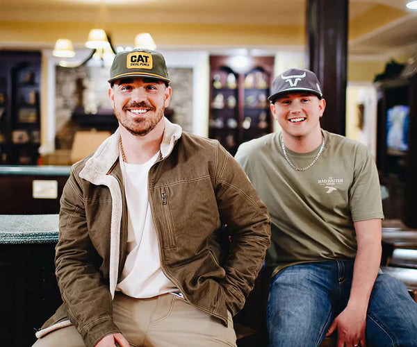 Two men sitting together in a bar or pub setting, wearing branded hats.